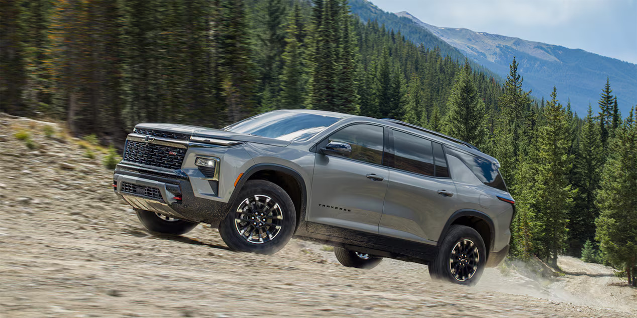 A gray 2024 Chevrolet Traverse driving up a hill.
