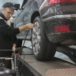 Serious car mechanic pumping up car wheel in modern service garage