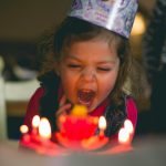 A little girl screams in excitement as she sits in front of her birthday cake with lit candles