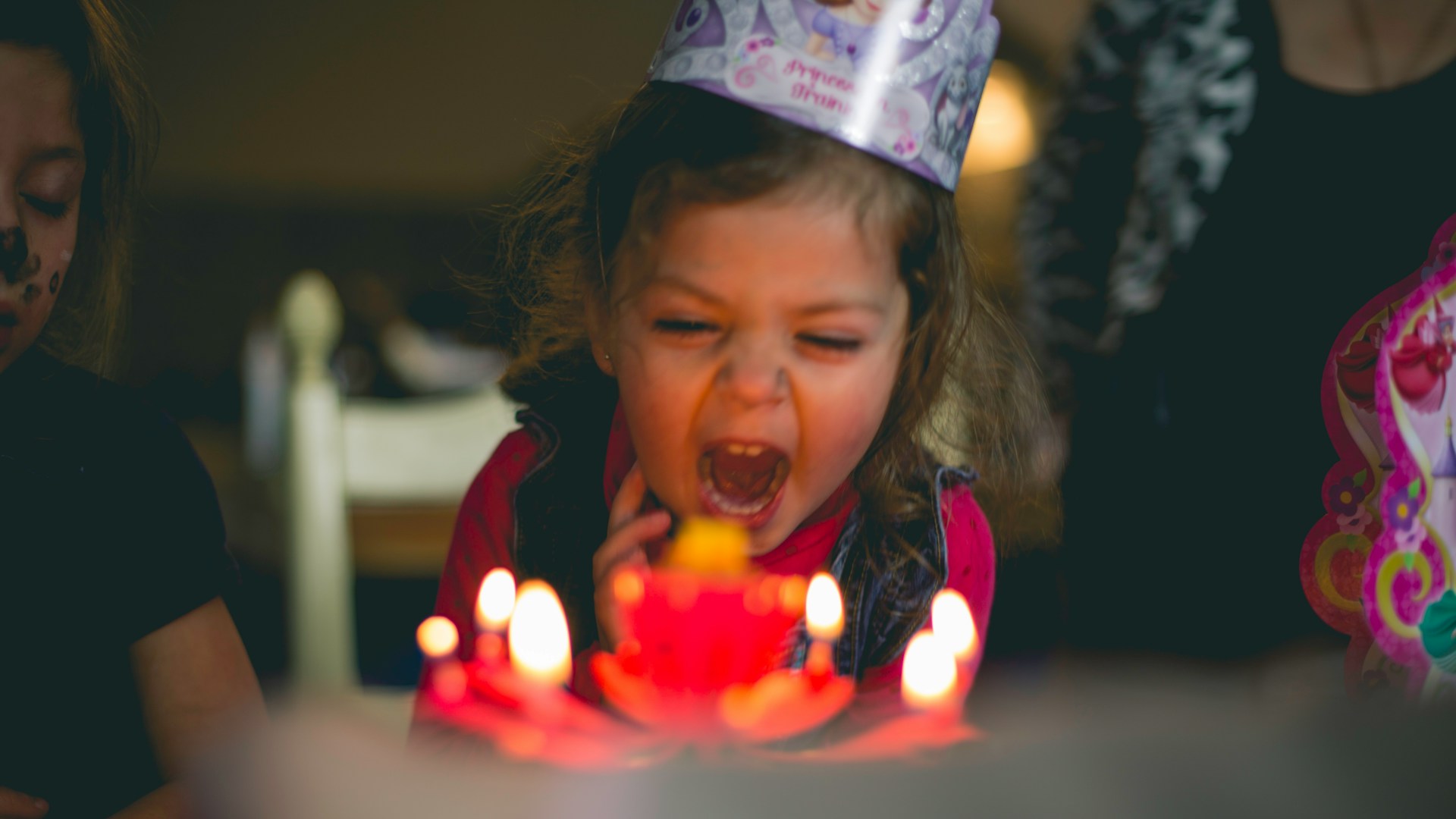 A little girl screams in excitement as she sits in front of her birthday cake with lit candles